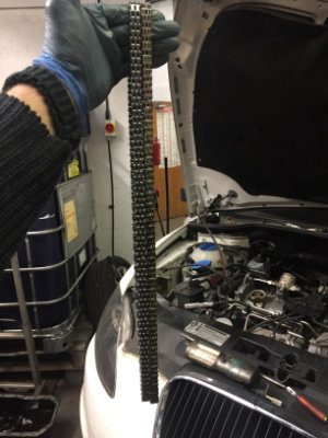 Hand holding a comparison between a new and worn timing chain.