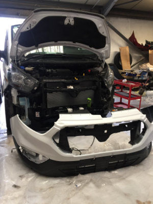 New front bumper placed in front of in-progress van repair, ready to be attached.